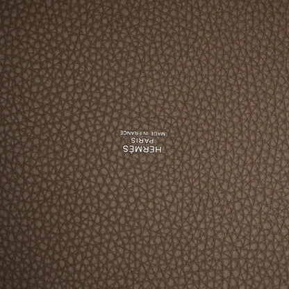 Taupe leather close-up with embossed “HERMES” stamp on textured calfskin.