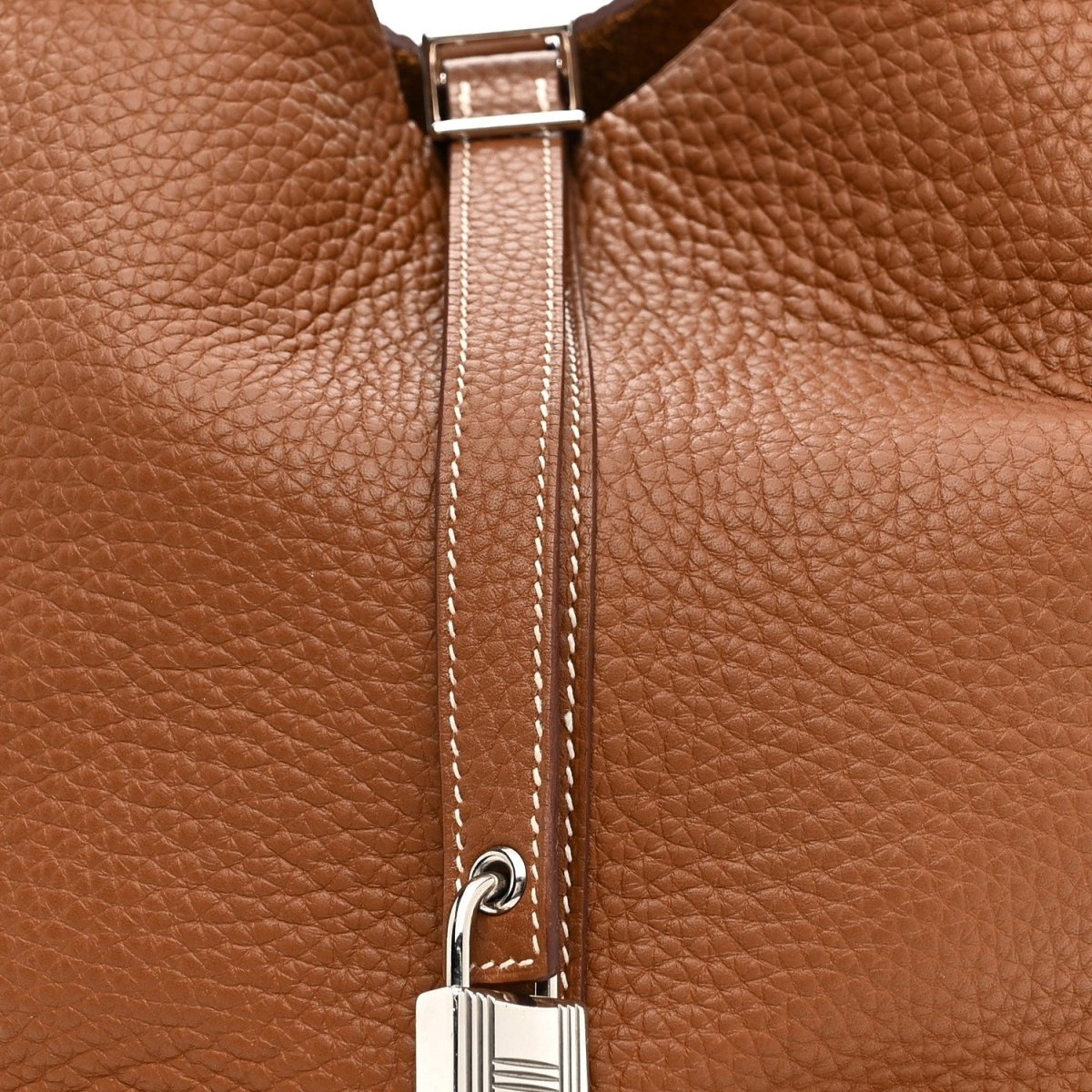 Gold leather tote bag zipper pull and metal clasp hardware detail