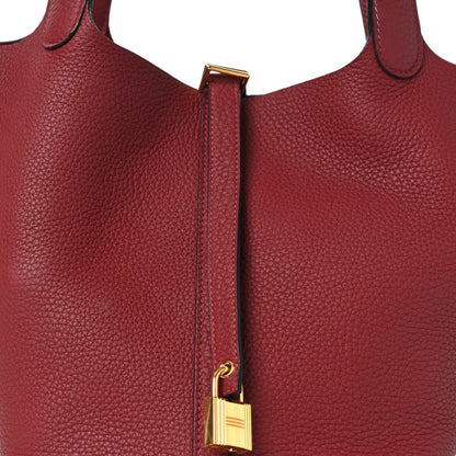 Red leather tote bag top lock clasp with gold hardware on front panel.