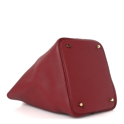Red leather tote bag corner with gold screws and reinforced side panel seam.
