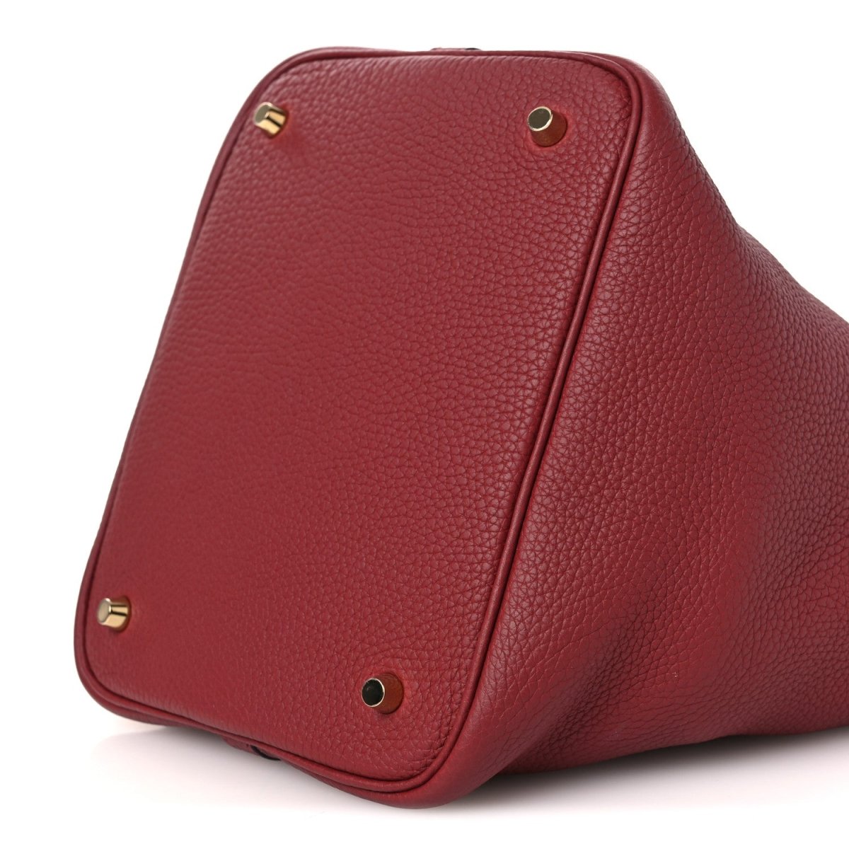 Red leather tote bag base corner with gold feet and rounded triangular shape.