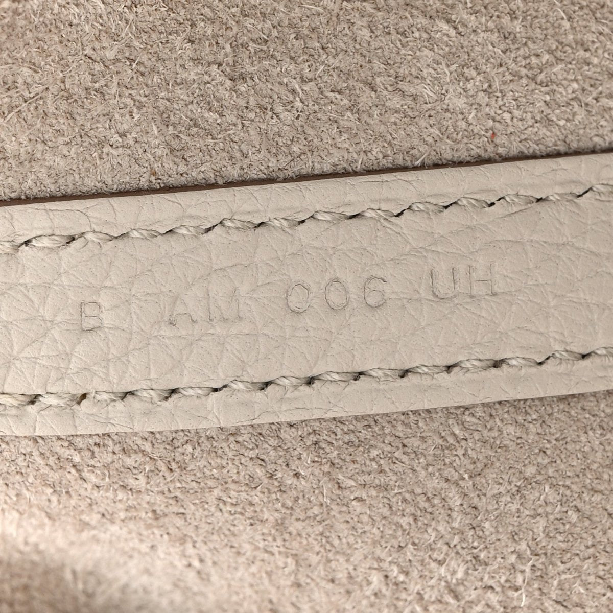 Off-white leather bucket bag seam with embossed maker marks and stitched edge