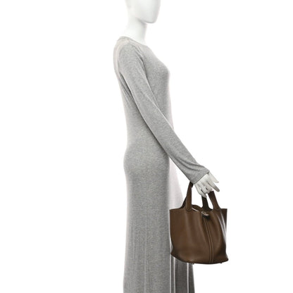 Taupe leather tote bag in hand with top handles, shown with gray sleeve