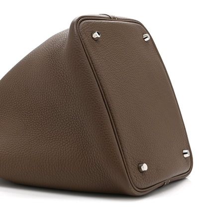 Taupe leather tote bag with top handle and metal stud closure on side panel
