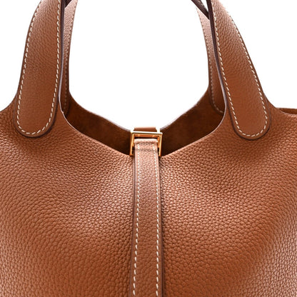Brown leather handbag front with top handles and gold lock zipper detail