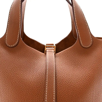 Brown leather handbag front with top handles and gold lock zipper detail