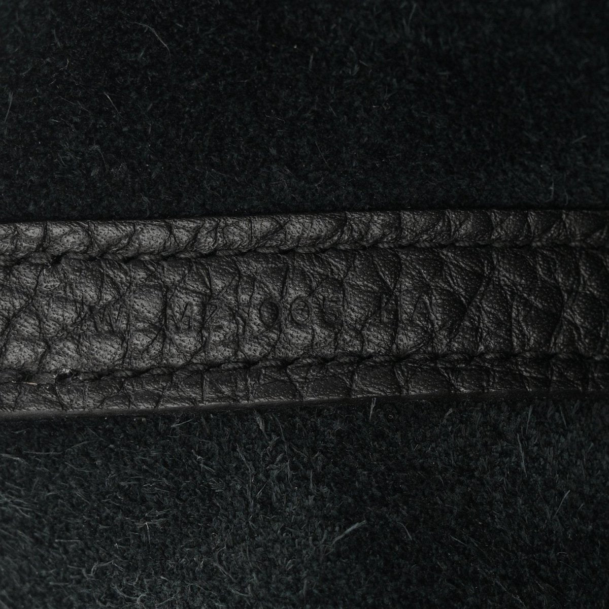 Black leather tote seam detail with pebbled texture and contrast stitching.