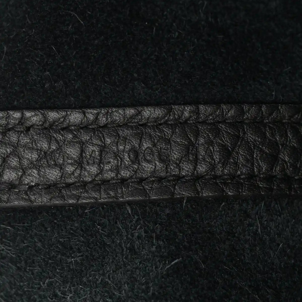 Black leather tote seam detail with pebbled texture and contrast stitching.
