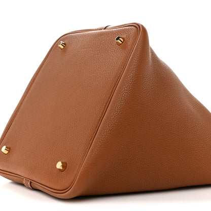 Tan leather tote bag with gold corner studs and folded side panel seam