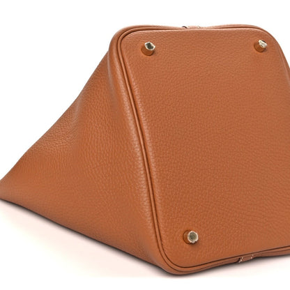Leather tote bag corner view with metal studs and piped seams, tan/brown.
