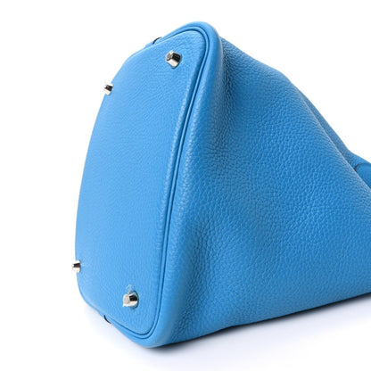 Blue leather tote bag with side lock hardware and curved handle panel, close-up