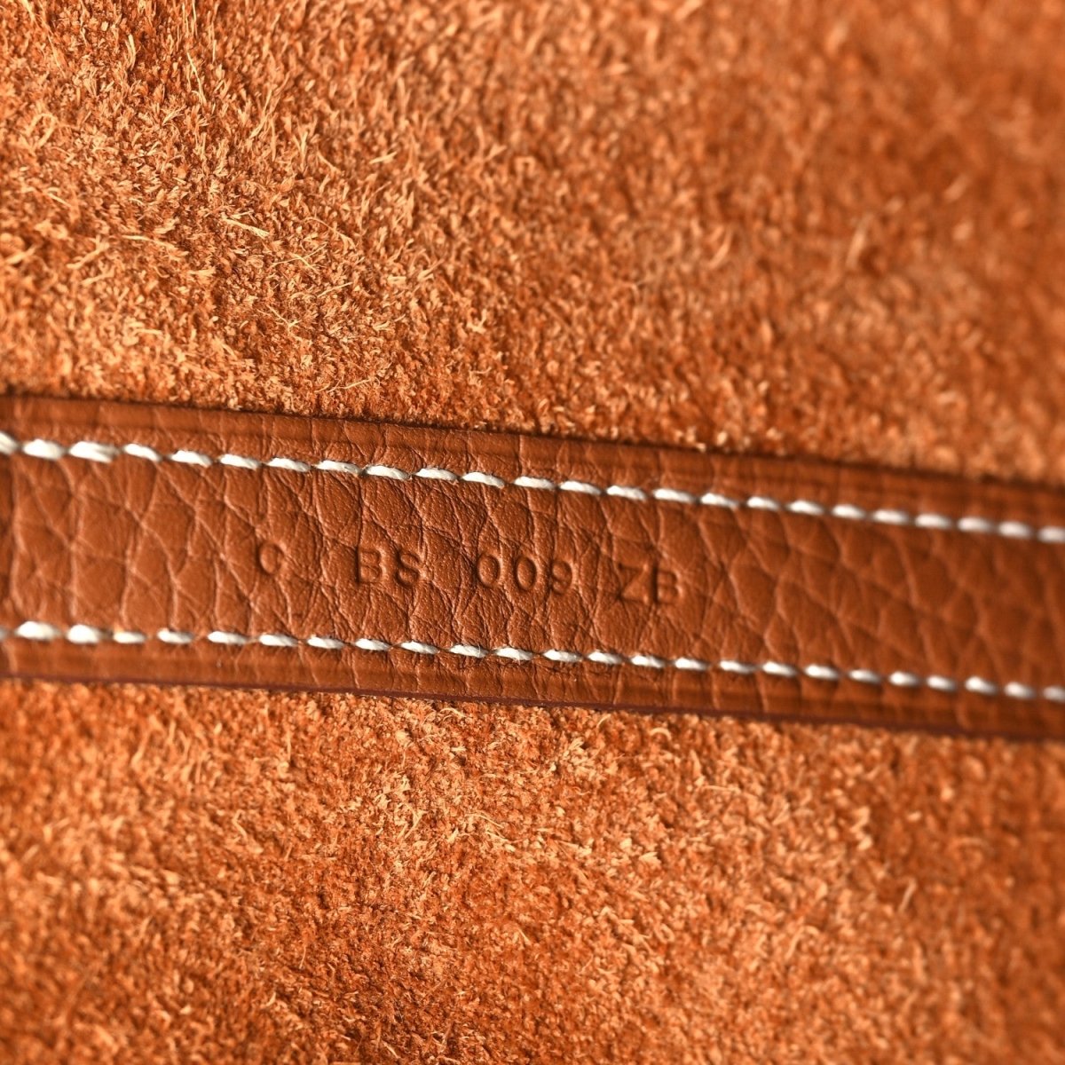Leather tote bag close-up of stitched strap with stamped code text