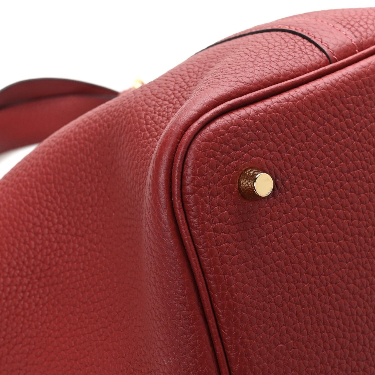 Red leather tote side close-up with round gold stud and curved edge