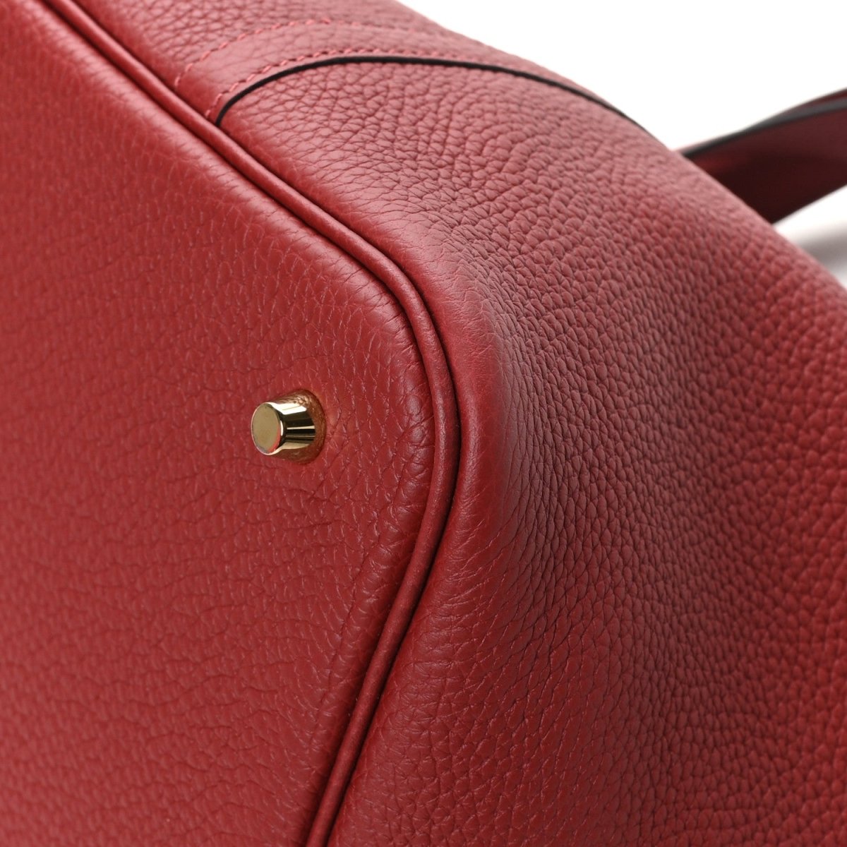 Red leather tote strap top close-up with round gold stud and seam