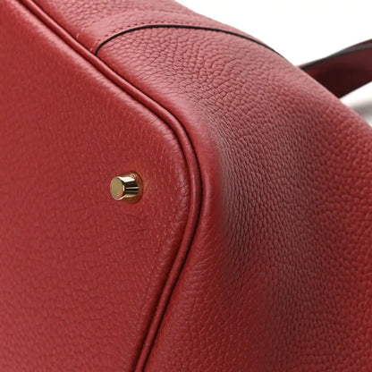 Red leather tote strap top close-up with round gold stud and seam