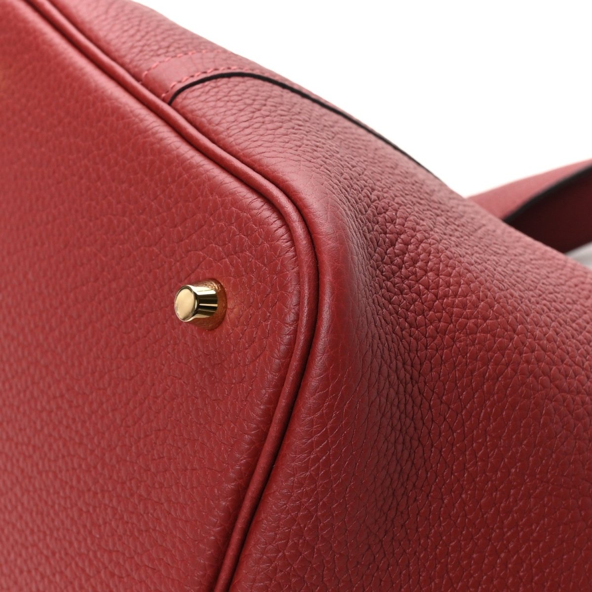 Red leather tote bag flap edge with gold clasp stud and textured grain