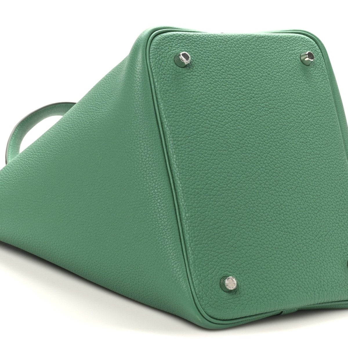 Green leather tote bag close-up with top corner hardware and textured grain