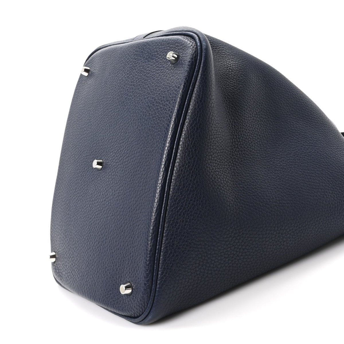 Navy leather tote bag end view with top handle, corner studs, curved base