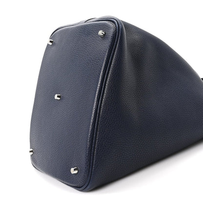 Navy leather tote bag end view with top handle, corner studs, curved base