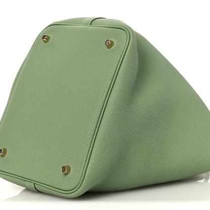 Green leather bucket bag side view with gold-tone studs on corner panels