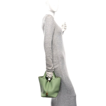 Green leather small bucket bag with top handles, held at side